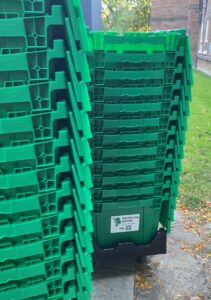 Stacks of green reusable moving boxes from “Mai Moving Rentals” on a dolly outside a Toronto building