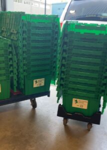 Stacks of green reusable moving boxes on rolling dollies from “Mai Moving Rentals” beside a delivery vehicle in Toronto
