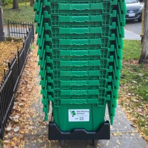 Stack of green reusable moving boxes on a delivery dolly from “Mai Moving Rentals” on a Toronto sidewalk.